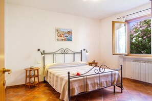 Een slaapkamer met een bed, nachtkastje, raam met uitzicht en een schilderij aan de muur.