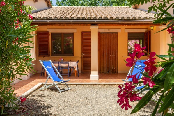 A villa with a tiled roof, a covered patio with a table and chairs, and two blue lounge chairs. - Agriturismo 'Trilo Begonia' with Pool, Wi-Fi & Garden (Marina di Grosseto)