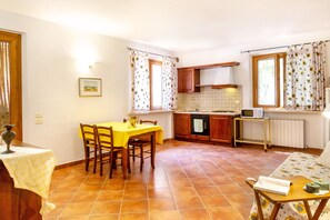 A kitchen with a dining table, chairs, a stove, and a window with curtains.