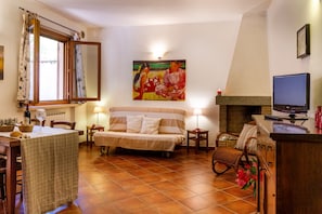 Ein gemütliches Wohnzimmer mit Sofa, Esstisch, Kamin und einem Gemälde an der Wand.