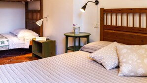Ein Schlafzimmer mit Etagenbett, Nachttisch mit Lampe, kleinem runden Tisch mit Vase sowie Bett mit gestreifter Bettwäsche und gemusterten Kissen.