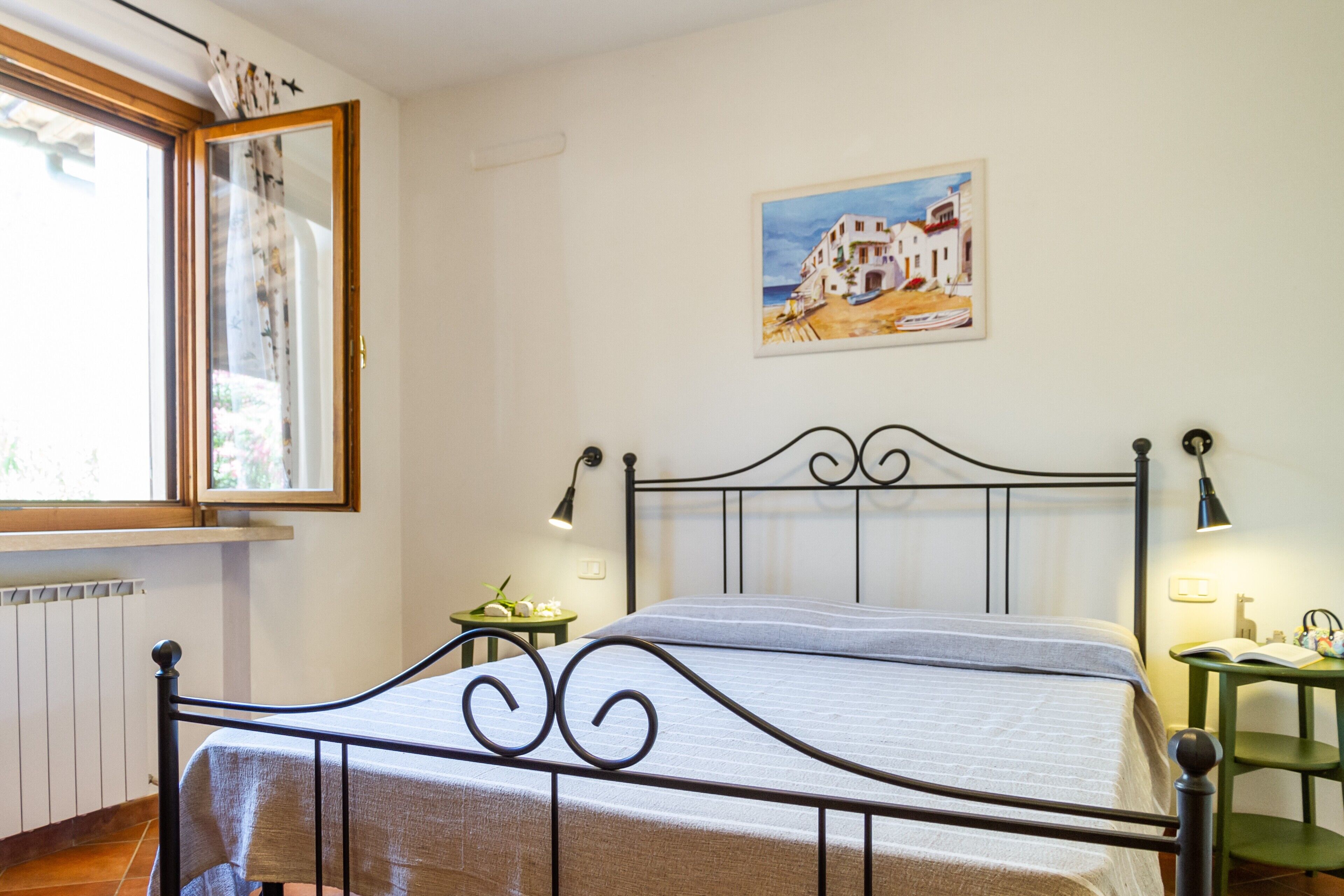 A bedroom with a bed, a window with curtains, a painting on the wall, and a bedside table with a lamp.