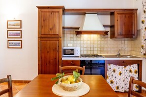 Een keuken met houten kastjes, een magnetron, een gasfornuis en een eettafel met stoelen.