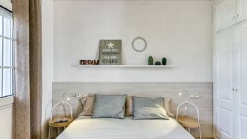 Ein Schlafzimmer mit einem Bett, Nachttischen, einem an der Wand befestigten Regal mit Dekoration und einem Fenster mit Vorhängen.