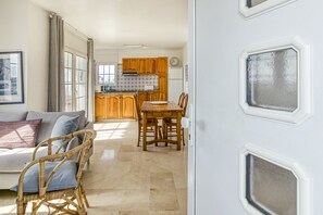 Une pièce comprenant un canapé, une table à manger avec des chaises, un coin cuisine avec des meubles en bois et une porte blanche agréée de panneaux de verre décoratifs.