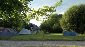 A campsite with several tents, a building, and surrounding trees.