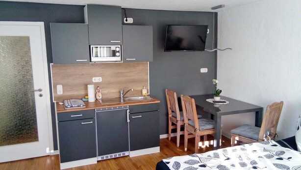 A compact room with a kitchenette, a dining area, and a TV mounted on the wall.