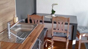A compact kitchen with a wooden countertop, stainless steel appliances, and a dining area with a wooden table and chairs.