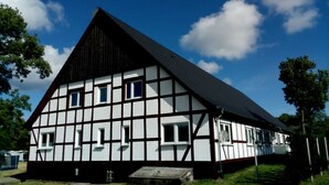 A traditional half-timbered building with a steep gable roof, multiple windows, and a small porch area.