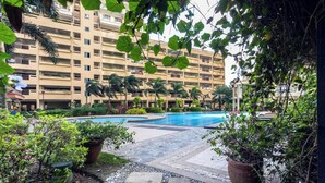 A multi-story building with a swimming pool surrounded by greenery and potted plants. - Couple's Getaway|Netflix|Fast net|Parking nr MAKTI (Mandaluyong)