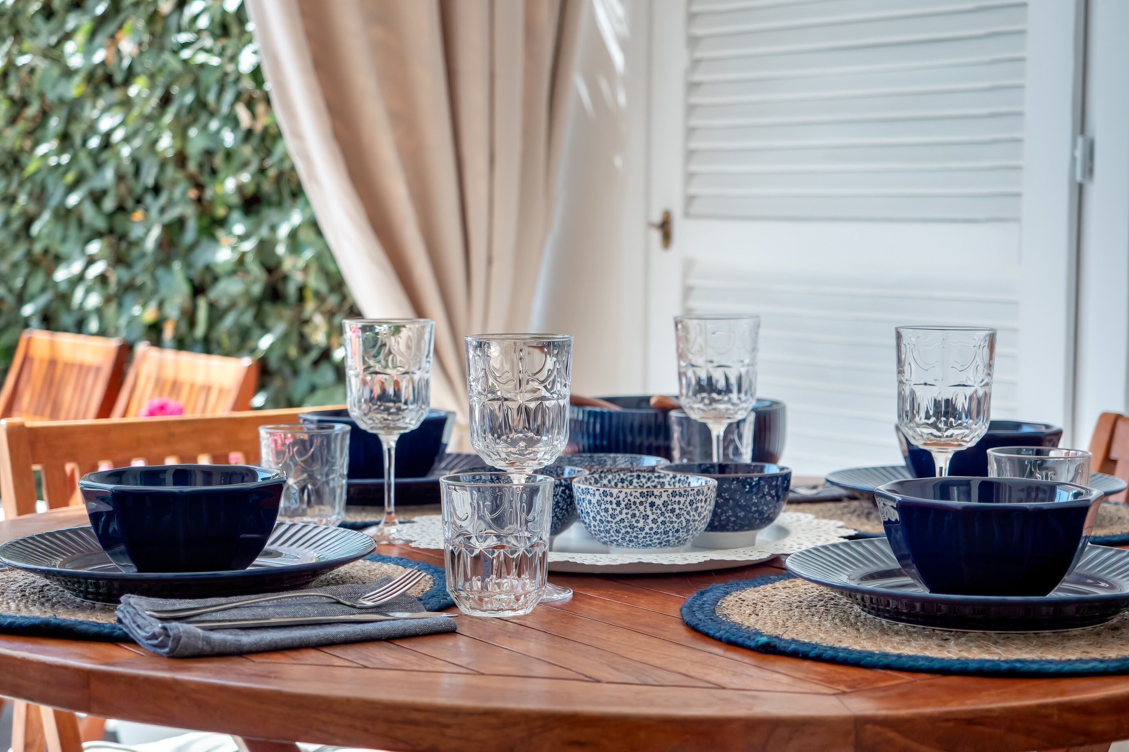 Une table à manger dressée avec de la vaisselle en verre bleue et transparente, des assiettes et des serviettes.