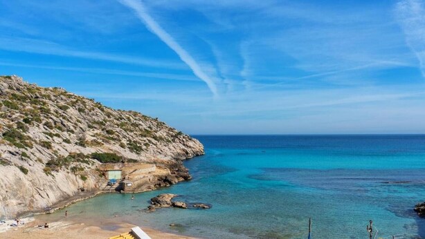 Un paysage côtier avec une eau d’un bleu limpide, un terrain rocheux et un petit bâtiment situé près du rivage.