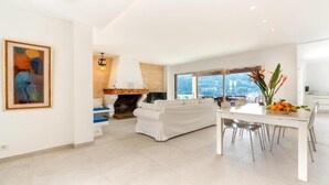 Un salon moderne avec une cheminée, un coin repas avec une table et des chaises, et une grande fenêtre offrant une vue dégagée.