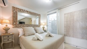 Ein Schlafzimmer mit einem großen Bett, zwei Nachttischen, einem Spiegel und einem Fenster mit Jalousien.