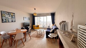 A modern living room with a dining area, a TV, and a large window with a view. - Beachfront Apartment with Balcony, Sleeps 4, 2 Stars (Les Sables-d'Olonne)