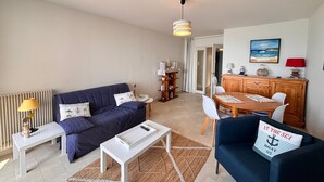 A living room with a sofa, coffee table, and dining area with chairs and a table. - Beachfront Apartment with Balcony, Sleeps 4, 2 Stars (Les Sables-d'Olonne)