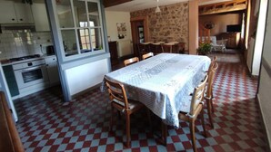 Une cuisine équipée d’une cuisinière, d’un four et d’une fenêtre. On y trouve également un coin repas avec une table et des chaises, et un mur en pierre en arrière-plan.