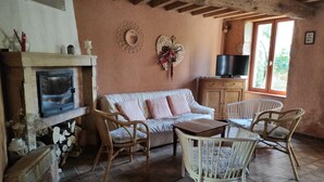Un salon chaleureux avec une cheminée, un canapé, des fauteuils en osier et un téléviseur.