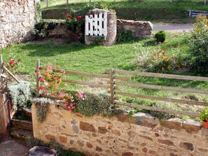 Un muro de piedra con una puerta de madera, un edificio de piedra y una zona cubierta de césped con flores.