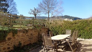 Une terrasse extérieure avec un mur en pierre, une clôture en bois et une table avec des chaises.