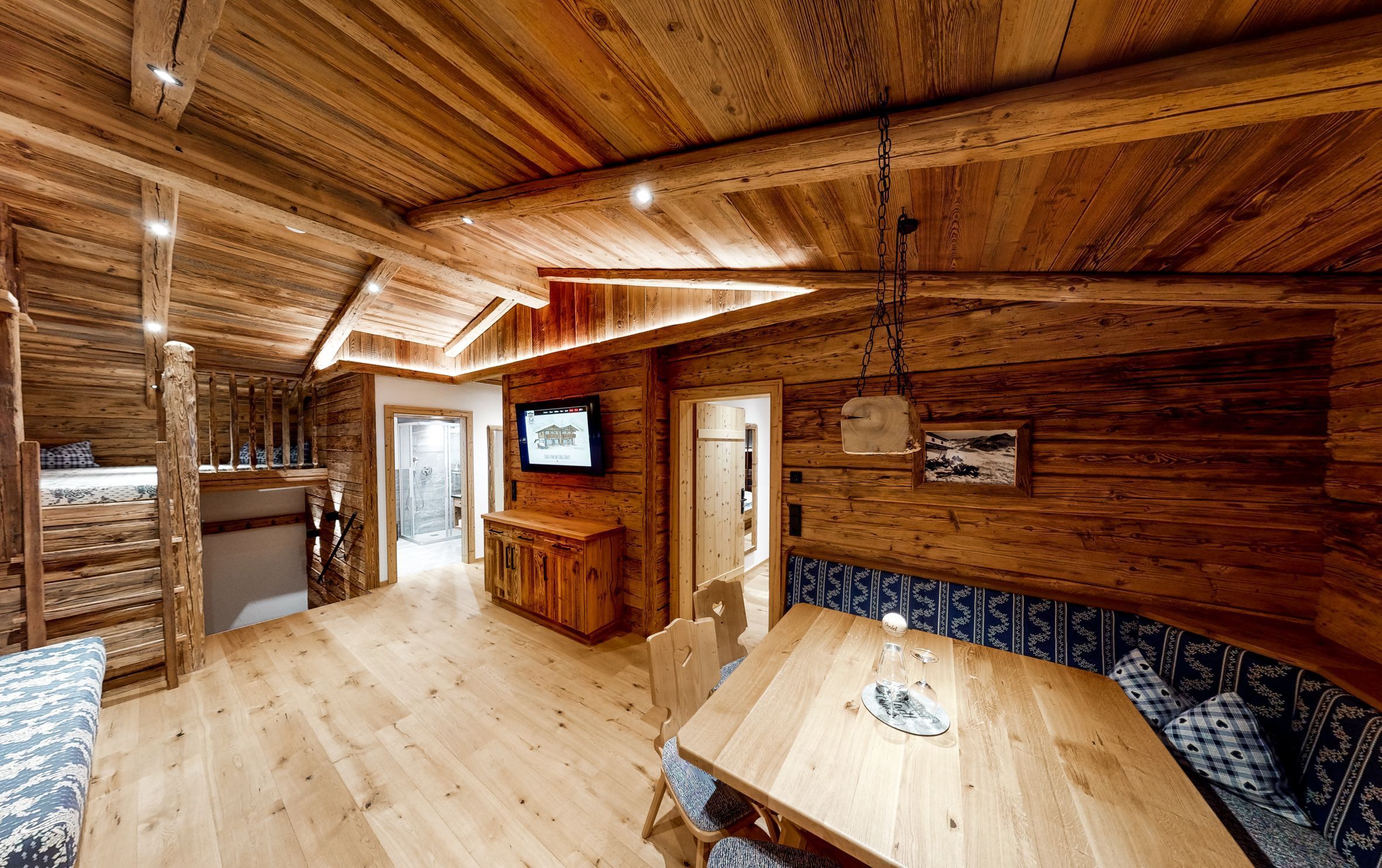 Een houten blokhut interieur met een eethoek, een aan de muur bevestigde televisie en een houten plafond.