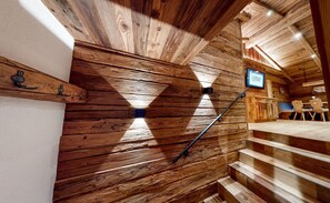 A wooden interior with a staircase, a mounted television, and a wall-mounted light fixture.