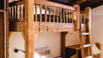 A rustic wooden bunk bed with a ladder, a small table, and a chair in a room with wooden flooring and exposed beams.
