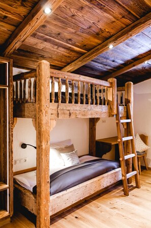 A rustic wooden bunk bed with a ladder, a small table, and a chair in a room with wooden flooring and exposed beams.
