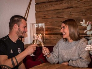 Deux personnes trinquent avec des coupes de champagne dans une pièce aux murs en bois, où un tableau encadré est accroché.