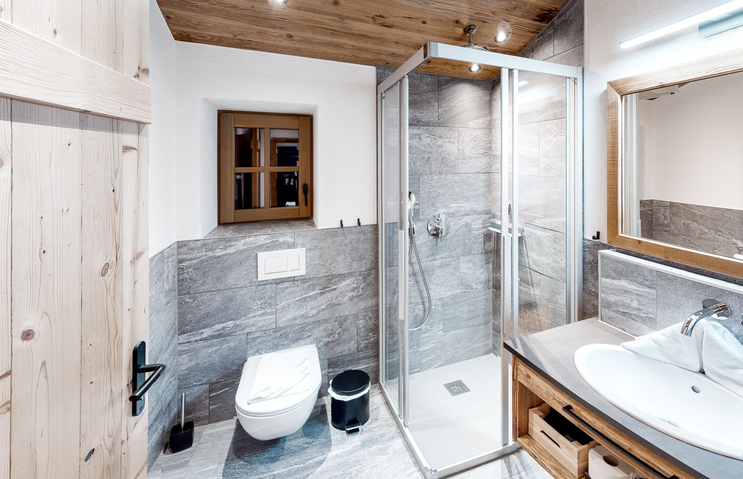 A modern bathroom with a glass shower enclosure, a white toilet, and a wooden vanity with a sink.
