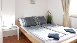A neatly made bed with patterned bedding, a bedside table with a lamp, a potted plant, and a framed picture on the wall. - Apartment city district 1 (Bremerhaven)