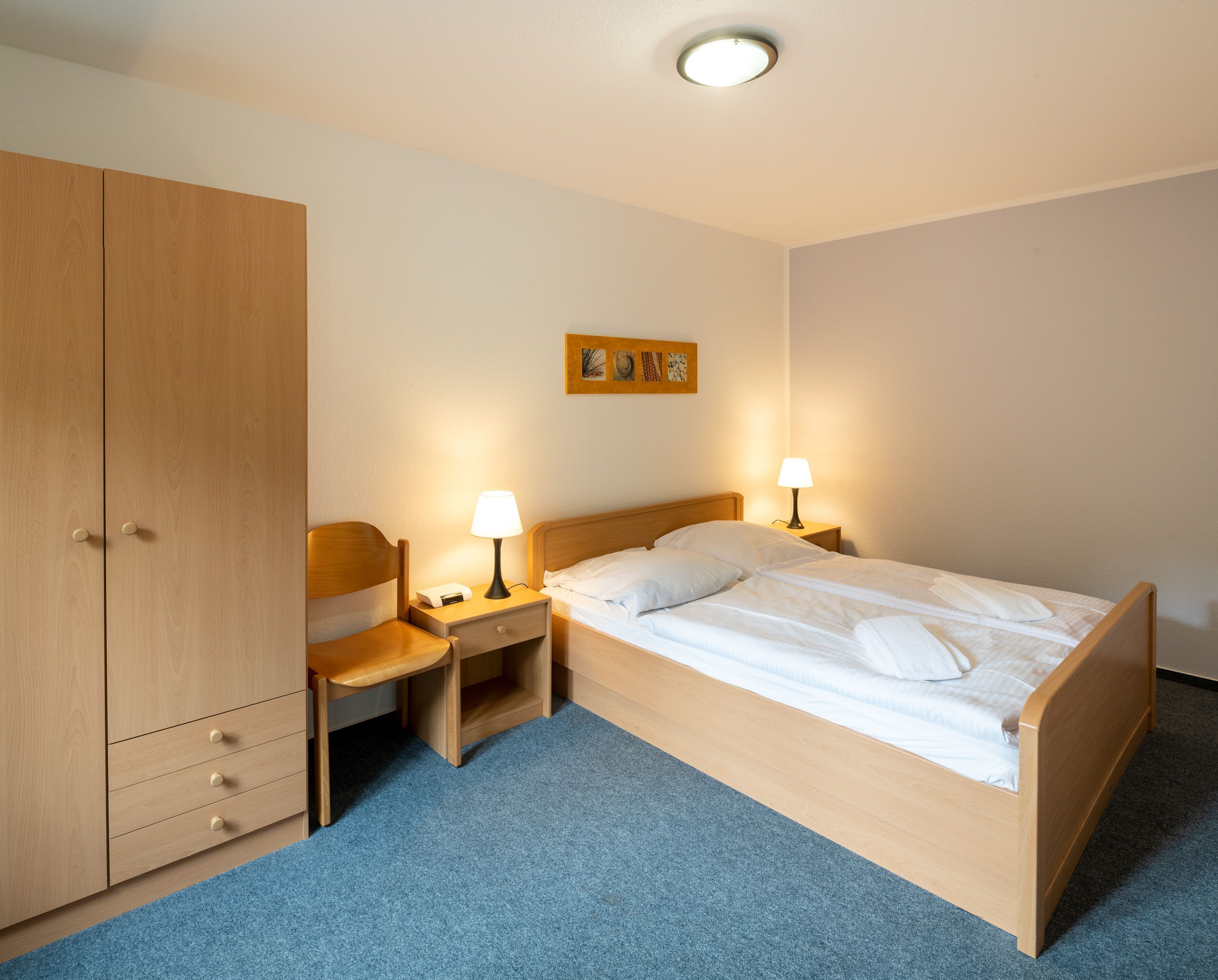 Ein Hotelzimmer mit einem hölzernen Bett, zwei Nachttischen mit Lampen, einem Holzschrank und einem blauen Teppich.