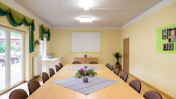 Een vergaderruimte met een lange tafel, stoelen, een projectiescherm en een raam met gordijnen.