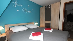 Una cama bien tendida con toallas blancas y rojas, un cabecero de madera y una pared verde azulado con la inscripción 'Gute Nacht' y estrellas.