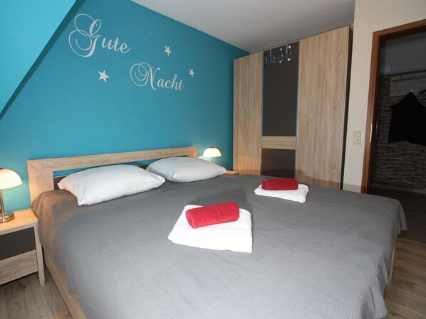 A neatly made bed with white and red towels, a wooden headboard, and a teal wall with the words "Gute Nacht" and stars.
