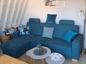 Un salon moderne avec un canapé d’angle, deux tables d’appoint et un lampadaire.