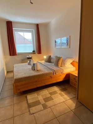 Une chambre à coucher avec un lit en bois, une fenêtre avec des rideaux, une table de chevet et un tapis à carreaux.