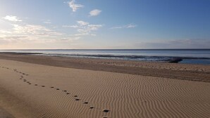 Ein Strand mit Fußspuren, die zum Wasser führen, ein klarer Himmel und ansteigende Wellen.