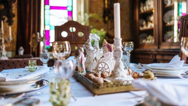 Una mesa de comedor dispuesta con vajilla de porcelana fina, cristalería y un centro de mesa decorativo.