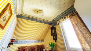 Una habitación con papel tapiz a rayas, techo estampado, un reloj de madera y una ventana con cortinas.