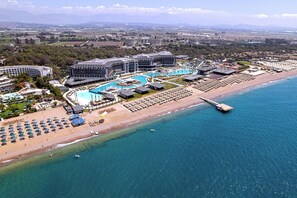 Luftaufnahme eines Küstenresorts mit großem Schwimmbecken, Strand und einer Pier.