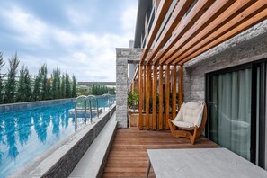 Ein moderner Poolbereich im Freien mit einer Holzterrasse, einer Liege und einer Steinmauer.