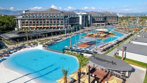 A hotel with multiple swimming pools, a large outdoor area with umbrellas, and a view of mountains in the background. - Lago Hotel (Manavgat)