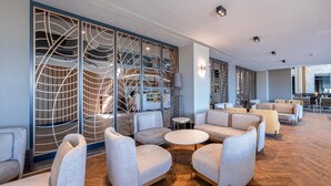 A modern lounge area with sofas and a coffee table, wooden flooring, and decorative screens. - Lago Hotel (Manavgat)