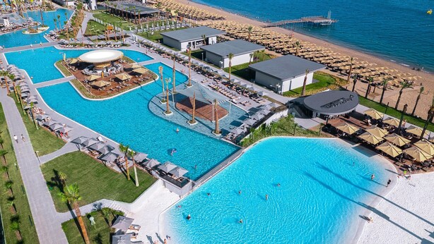 An aerial view of a resort with multiple swimming pools, a beach area, and beach umbrellas. - Lago Hotel (Manavgat)