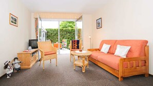 A room with a sofa, chairs, a small table, a television, and a view through a glass door. - Vacation apartment Riegstra in Esens - Holiday apartment Riegstra (Esens)