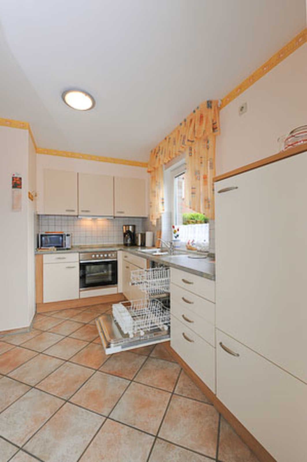 A compact kitchen with white cabinets, a microwave, an oven, a dishwasher, and a window with curtains.