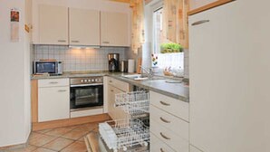 A compact kitchen with white cabinets, a microwave, an oven, a dishwasher, and a window with curtains. - Vacation apartment Riegstra in Esens - Holiday apartment Riegstra (Esens)