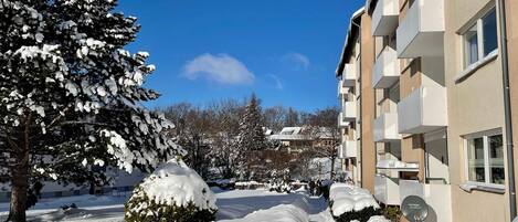 A snow-covered residential area with a building featuring balconies and a clear blue sky.