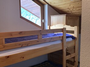 Uma cama de beliche com janela acima, um guarda-roupa de madeira e teto inclinado.